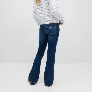 Blå bootcut jeans från Gina - Snygga blå bootcut jeans med klassiska bakfickor med lock och knapp. Jeansen har en mörk tvätt och markerade sömmar, vilket ger en stilren och trendig look. 