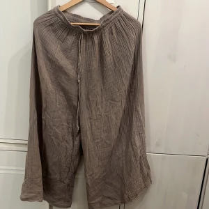 Beiga vida bomullsbyxor med snörning - Superbekväma och luftiga bomullsbyxor i beige med bred passform och resår i midjan. Byxorna har snörning i midjan och ett snyggt, krinklat tyg som ger en avslappnad vibe. Perfekta för varma dagar eller när du vill chilla hemma.