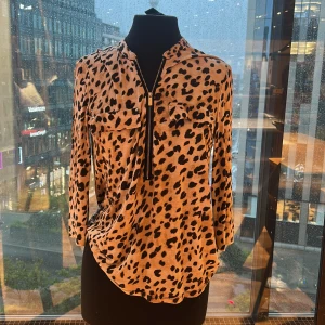Leopardmönstrad skjorta Calvin Klein - Snygg leopardmönstrad skjorta från Calvin Klein i beige och svart. Skjortan har lång ärm, två bröstfickor med knappar och en dragkedja framtill. Mjuk och skön känsla, perfekt för dig som vill se professionell ut