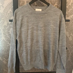 Grå merinoulltröja från Sandö - En stilren grå tröja från Sand i mjuk merinoull. Klassisk rund halsringning och långärmad modell, perfekt för lager-på-lager. Enkel och tidlös design som funkar till det mesta. Storlek L sitter mer som S-M. Skriv vid minsta lilla fundering!