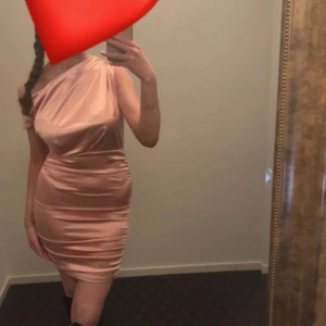 Champagnefärgad one shoulder klänning - Snygg kort klänning i champagnefärgat satinliknande material med one shoulder-design. Tight passform som framhäver figuren och ger en elegant look. Perfekt för dig som vill sticka ut med en stilren och trendig outfit.