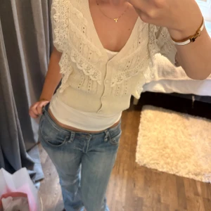 Beige spetskofta från Zara - Supersöt beige kofta från Zara med kort ärm, v-ringning och knappar framtill. Stickad i mjukt material med detaljer av spets och volanger över axlar och bröst. 