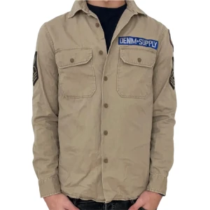 Beige overshirt från Denim & Supply - Snygg beige overshirt från Denim & Supply med coola patchar på ärmarna och bröstet. Skjortan har två bröstfickor med lock och knappar framtill. Perfekt för dig som gillar en avslappnad och trendig stil.