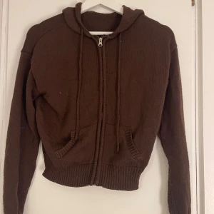 Brun hoodie med dragkedja, strl M - Mysig brun hoodie med huva och dragkedja framtill. Tröjan har långa ärmar, ribbade muddar och två fickor fram. 