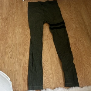 Gröna leggings med svarta ränder - Mörkgröna leggings med bred midja och två svarta ränder över ena låret. Stretchigt material som sitter tight och bekvämt. Perfekta för träning eller chill. Ribbad struktur nedtill på benen för extra stil.