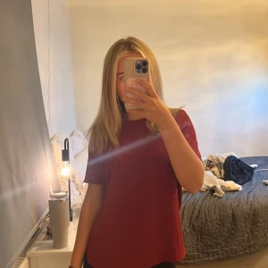 Vinröd glittrig blus från Vero Moda - Vinröd blus från Vero Moda med glittriga detaljer och struktur i tyget. Blusen har korta ärmar och en snygg guldig dragkedja i ryggen. Perfekt för dig som vill ha något enkelt men ändå med lite extra shine.