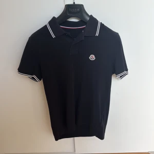 Moncler pikétröja -  En unik och riktigt schysst mörkblå Moncler piké i st 2/Small för endast 1200kr! Nypris 3600kr. 