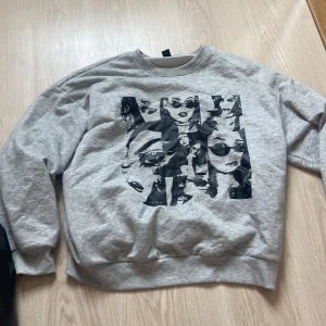 Grå sweatshirt med svart tryck - Grå sweatshirt med coolt svart tryck av ansikten på framsidan. Tröjan har rund halsringning och långa ärmar. Perfekt för dig som gillar streetstyle och vill sticka ut med ett unikt motiv.