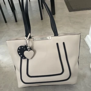 Beige axelväska från Guess med hjärtberlock - Rymmer mycket aldrig använt