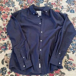 Mörkblå skjorta från 157, storlek L - Snygg mörkblå skjorta från 157 i storlek L. Skjortan har klassisk krage, vita knappar och långa ärmar med manschett. Perfekt för dig som gillar en stilren och enkel look. Materialet känns mjukt och bekvämt mot huden.