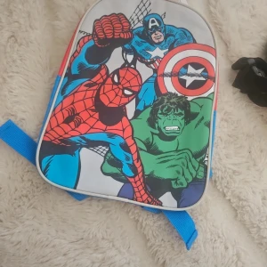 Marvel ryggsäck med superhjältar - Cool ryggsäck med tryck av Spiderman, Captain America och Hulk på framsidan. Väskan har blåa axelband, röd baksida och insida samt vita och blå detaljer. Perfekt för dig som älskar Marvel och vill sticka ut med färgglad design.