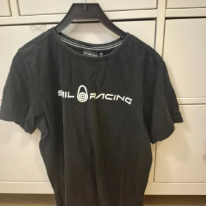Svart Sail Racing t-shirt i bomull - Svart t-shirt från Sail Racing med vit logga tryckt på bröstet. Modellen heter JR Bowman Tee och är tillverkad i 100% bomull.