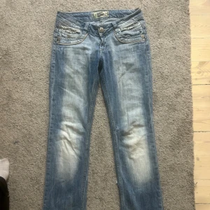 Ljusblå jeans med nitar och broderi - Skit snygga ljusblå jeans från Victoria Beckham med slitningar och coola detaljer. Jeansen har låg midja och utsvängda ben, samt dekorativa sömmar och metallknappar. Tyvärr är dom försmå för mig. Kan gå ner i pris 