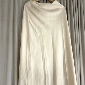 Lång vit kjol i satin - Säljer en elegant långkjol i vit satin med slät yta och lätt glans. Kjolen har en enkel och stilren design utan mönster eller detaljer, perfekt för dig som gillar minimalistisk stil. Den har en bred linning som ger en snygg siluett.