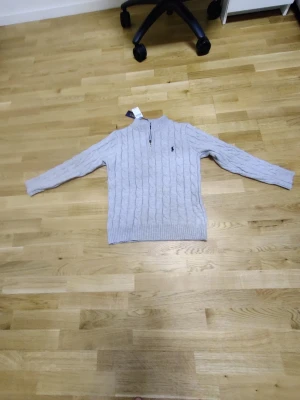 tröja Polo Ralph Lauren - Ljusgrå kabelstickad tröja från Polo Ralph. Den är helt ny. Säljer den på grund av att det är fel storlek och ni kan se det på bilden hur korta armar och tajt den är. 