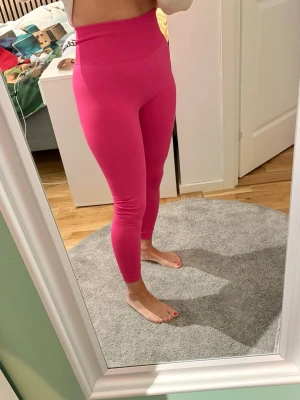 Höga rosa träningstights - Säljer ett par snygga, träningstights i stark rosa färg. De har en tight passform och bred midjeresår. Perfekta till träning. Materialet är stretchigt och följsamt. Aldrig använda. Märket är Wear Balance