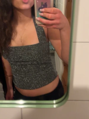 Fest topp - Snygg glittrig svart topp med croppad passform och breda axelband. Perfekt för dig som vill sticka ut lite extra. Toppen har en fyrkantig urringning och sitter tight mot kroppen.