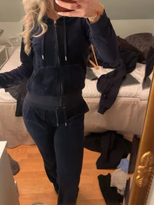 Mörkblå juicy couture - Mysigt mörkblått juicy couture sett med dragkedja framtill, huva och snörning i midjan. Setet består av en zip hoodie och matchande byxor med fickor därbak och ribbade muddar. Perfekt för chill dagar hemma. Storlek S i zipen och storlek XS i byxorna