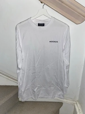 Vit långärmad tröja från McKenzie - Vit långärmad tröja från McKenzie med rund halsringning och diskret svart logotyp på bröstet. Tröjan är i ett mjukt och lätt material, perfekt för en clean och enkel stil. Aldrig använd, storlek S