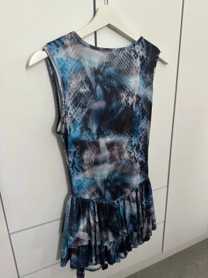 Blå mönstrat playsuit - Jättefin playsuit i blå/lila/svart/vit med volangdetaljer längst ner.  Endast använd under 1 dag.