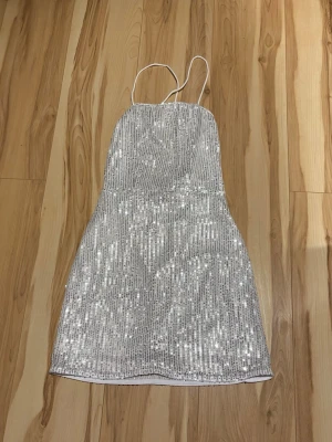 Silverglittrig paljettklänning från SHEIN - Kort klänning med smala axelband och öppen rygg med snörning. Helt täckt av silvriga paljetter, figurnära passform och lätt utsvängd nederdel.