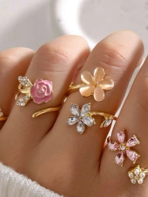 Blommiga guldringar med stenar 4 stycken  - Flera trendiga guldfärgade ringar med blommotiv och gnistrande stenar. Ringarna har detaljer i rosa, vitt och guld, vissa med emaljerade blommor och andra med kristallstenar. Perfekt för dig som gillar söta och unika accessoarer.