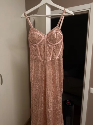 Helt ny rosa balklänning  - Säljer en superfin långklänning i ljusrosa med glittriga paljetter över hela klänningen. Klänningen har smala axelband, markerad byst och figurnära passform upptill. Perfekt för dig som vill sticka ut med en glamorös look. Helt ny och säljs pga att den var för stor. Är i storlek 32 men är som en 34 därav angiven storlek.
