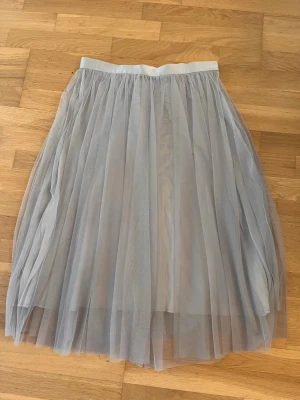 Ida Sjöstedt kjol strl 40 - Grå kjol från Ida Sjöstedt i strl 40.  I nyskick.  Knäppen i sidan. Obs, knäppet längst ner går ej att knäppa. Var så vid köp. Se bild nr 5 för närbild.  Mått midja mätt rakt över ca: 40-41 cm Total längd kjol: ca 39 cm.  