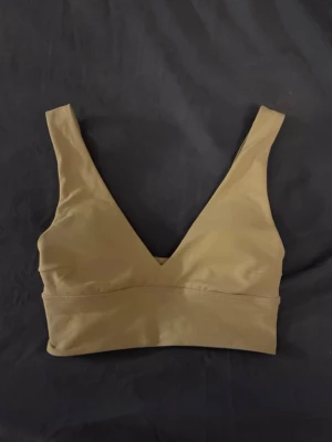 Beige sport-bh från Lululemon - Snygg beige sport-bh från Lululemon med djup v-ringning och breda axelband. Tillverkad i ett mjukt och stretchigt material som ger bra stöd vid träning. Perfekt för gymmet eller yoga.