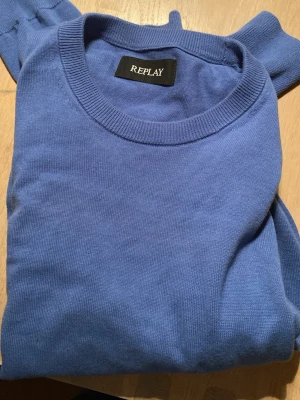 Blå stickad tröja från Replay - En stilren blå stickad tröja från Replay med rund halsringning och ribbade muddar. Tröjan har en klassisk passform och är perfekt för lager-på-lager. Materialet känns mjukt och bekvämt mot huden.