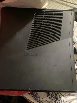Xbox 360 Slim spelkonsol svart - Säljer en svart Xbox 360 Slim spelkonsol från Microsoft. Konsolen har en stilren, matt finish och ventilerad ovansida för bättre kylning. Den klassiska designen gör den enkel att placera i tv-bänken och den är tillverkad i plast.