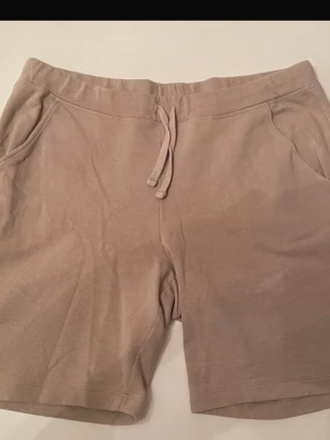 Beige shorts med snörning, Kappahl storlek L - Mysiga beige shorts med snörning i midjan och två sidofickor. Perfekta för varma dagar eller chill hemma. Tillverkade i mjukt material för extra komfort och avslappnad passform. 