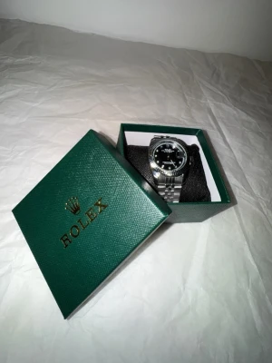 Silverklocka - Snygg herrklocka i silver med svart urtavla och datumvisning. Klockan har en klassisk länkarmband i metall och urtavlan är dekorerad med glittriga indexmarkeringar. Kommer i original grön box.