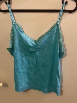 Ljusblå ribbad linnetopp Bik Bok - Supersöt ljusblå ribbad linnetopp från Bik Bok med spetsdetaljer längs v-ringningen och tunna axelband. Toppen har en lätt rynkning framtill och är perfekt för varma dagar eller som layering-piece.