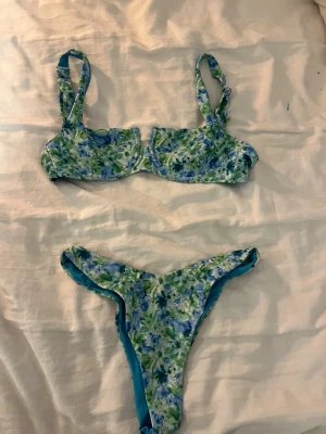 Blommig bikini i blått och grönt - Bikini med blommigt mönster i blått, grönt och vitt. Överdelen har breda axelband och även bygel, underdelen är ganska vanlig med relativt hög skärning. 💚🩵