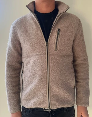 Beige teddyjacka från John henric, stolek S - Mysig beige teddyjacka med hög krage och hel dragkedja framtill. Jackan har tre fickor med dragkedja, en på bröstet och två på sidorna. Tillverkad i fluffigt teddy-material som ger en avslappnad och trendig look.