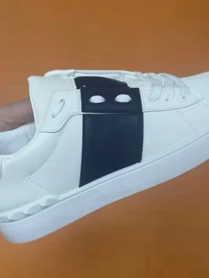 Vita sneakers med svart detalj - Stilrena vita sneakers med bred svart läderdetalj över snörningen. Skorna har vita skosnören och en klassisk låg siluett. Sulan är vit och ovandelen är i slätt material, troligen konstläder. Perfekta för en clean och modern look.