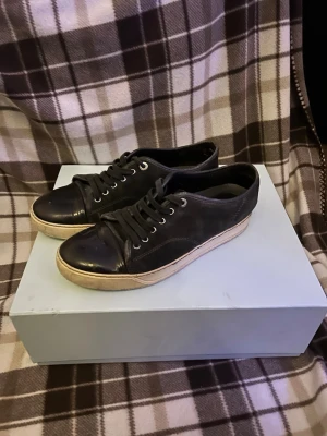 Svarta sneakers från Lanvin - Stilrena svarta sneakers från Lanvin med ovandel i mocka och tåparti i blankt skinn. Skorna har vita sulor och klassisk snörning med metallöljetter. Perfekta för dig som gillar en clean och tidlös look.Kom med frågor allt og!🙌👍Fel sula inom det är en svart sula inte lanvins därför detta pris kom dm om ni vill ha frågor eller bild på skon eller sulan 🙌🙌🥳