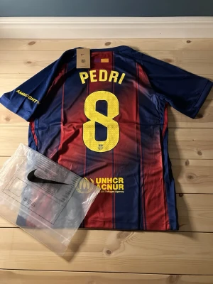 FC Barcelona matchtröja Pedri #8 - Säljer en officiell FC Barcelona matchtröja från Nike med Pedri och nummer 8 på ryggen. Tröjan är blå och röd med gula detaljer, klubbmärke och Spotify-logga på bröstet. Tillverkad i lätt och ventilerande material, perfekt för fotboll eller träning.