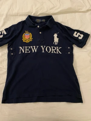 Chief keef polo new york - Marinblå pikétopp med krage från Polo Ralph Lauren. Stora broderade detaljer med vit polospelare, texten 'NEW YORK' och gult emblem på bröstet. Nummer 5 på ärmarna. Klassisk passform i bomull perfekt för dig som vill ha en skön stil