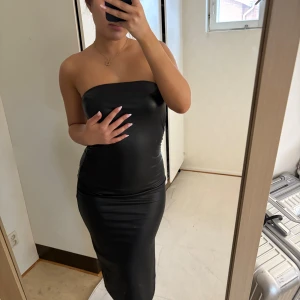 Svart axelbandslös långklänning - Säljer en svart, axelbandslös långklänning i figurnära modell. Klänningen har en stilren och elegant design med slät yta och är perfekt för dig som gillar en minimalistisk look. Materialet känns mjukt och följsamt mot kroppen.