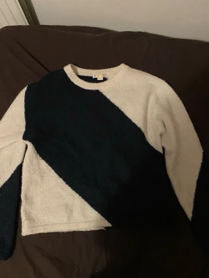 Svartvit stickad tröja med diagonal design - Snygg stickad tröja i svart och vitt med coolt diagonalt mönster. Tröjan har rund halsringning och långa ärmar. Perfekt för dig som gillar en stilren men ändå unik look.