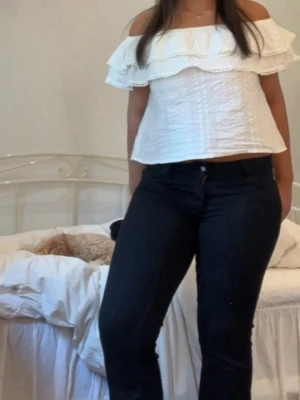 Vit offshoulder volangtopp - Superfin vit offshoulder topp med volangdetaljer och bred resår upptill. Toppen är croppad och har en luftig passform, perfekt för varma dagar. Materialet känns som bomull och ger en lätt och fräsch känsla.