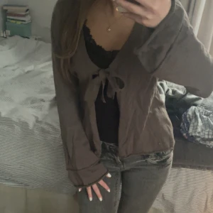 Beigegrå omlottkofta med knytband - Supersöt brun omlottkofta med långa ärmar och knytband framtill. Koftan har en avslappnad passform och är perfekt att slänga över ett linne eller topp. Mycket bra skick, nästan helt ny. Fina detaljer på ärmar och sida i väldigt bra kvalitet. Materialet känns mjukt och lätt, vilket gör den perfekt till våren eller sommaren!💕🌷