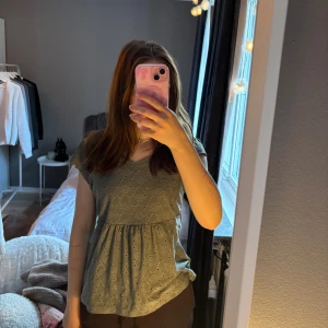 Grön blus  - Säljer en söt grön blus med broderade hålmönster och v-ringad hals. Blusen har korta ärmar och en lätt rynkad midja 💘