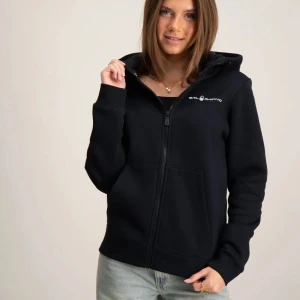 Svart hoodie från Sail Racing - Svart hoodie från Sail Racing med dragkedja framtill och vit logga på bröstet. Tröjan har huva, känguruficka och långa ärmar. Perfekt för en avslappnad stil och enkel att matcha med jeans eller joggers.