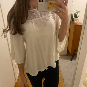 Vit blus med spets och öppen rygg - Säljer en luftig vit blus med trekvartsärm och vackra spetsdetaljer upptill. Blusen har öppen rygg med knytband och en lös passform som ger en avslappnad känsla. Från Pull&Bear 