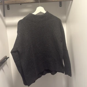 Mörkgrå stickad tröja från Uniqlo - Mysig mörkgrå stickad tröja från Uniqlo med hög hals och avslappnad passform. Perfekt för lager-på-lager och chill höst- och vinterstil. Långa ärmar och mjukt material som håller dig varm hela säsongen.