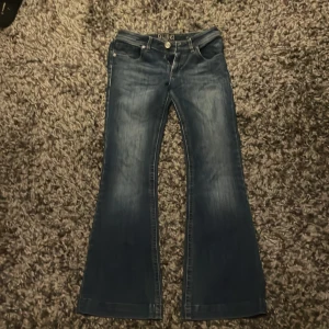 Blå bootcut jeans DL1961 Joy - Snygga blå jeans från DL1961 i modellen Joy med bootcut. Jeansen har klassisk femficksdesign, ljusare tvätt på låren och subtila slitningar. Materialet är mjukt denim med stretch för extra komfort. Perfekta för dig som gillar en retroinspirerad look.