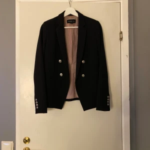 En mörk blå karvaij från mango  - En väldigt stilren och elegant mörk blå kavaj från mango säljs.Är helt oanvänd och passar till allt är även väldigt häftig med sina knappar på kavajens ärmar och vid nedanför bysten.Frakt ingår inte 